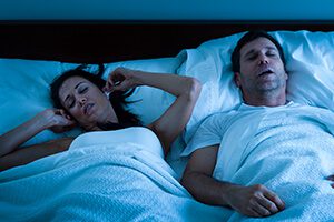 Couple sleeping in bed while a man experiences snoring and sleep apnea symptoms during the night.